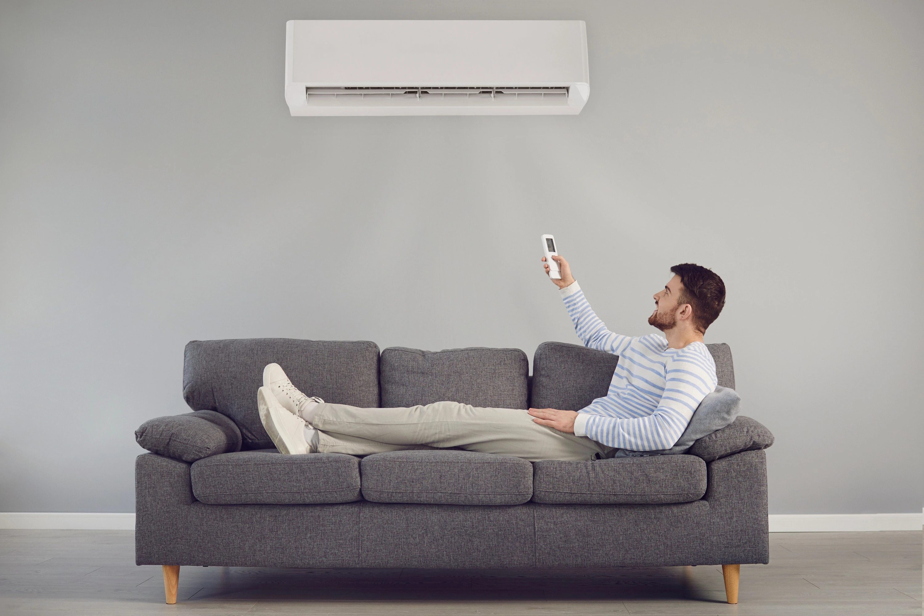 Homme allongé sur un canapé, télécommande à la main, profitant de sa climatisation réversible installée par Eneoji